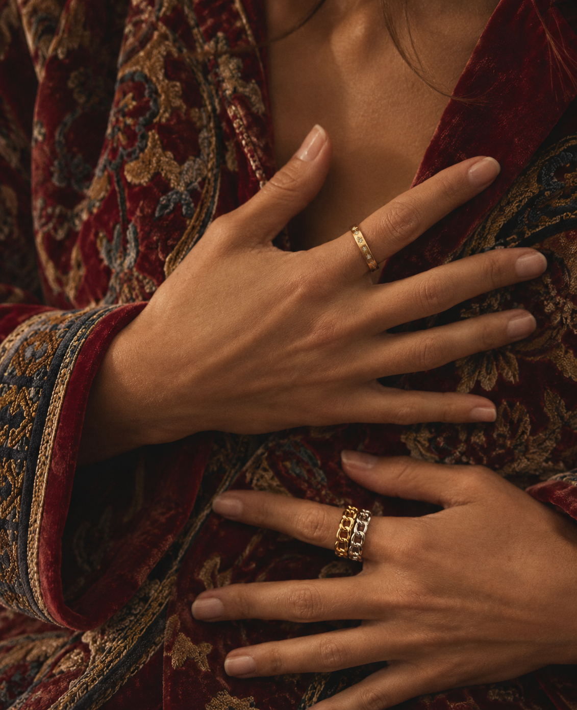 Hands on a red embroidered velvet jacket wearing diblin chain rings in gold and silver and a gold CZ stacker ring